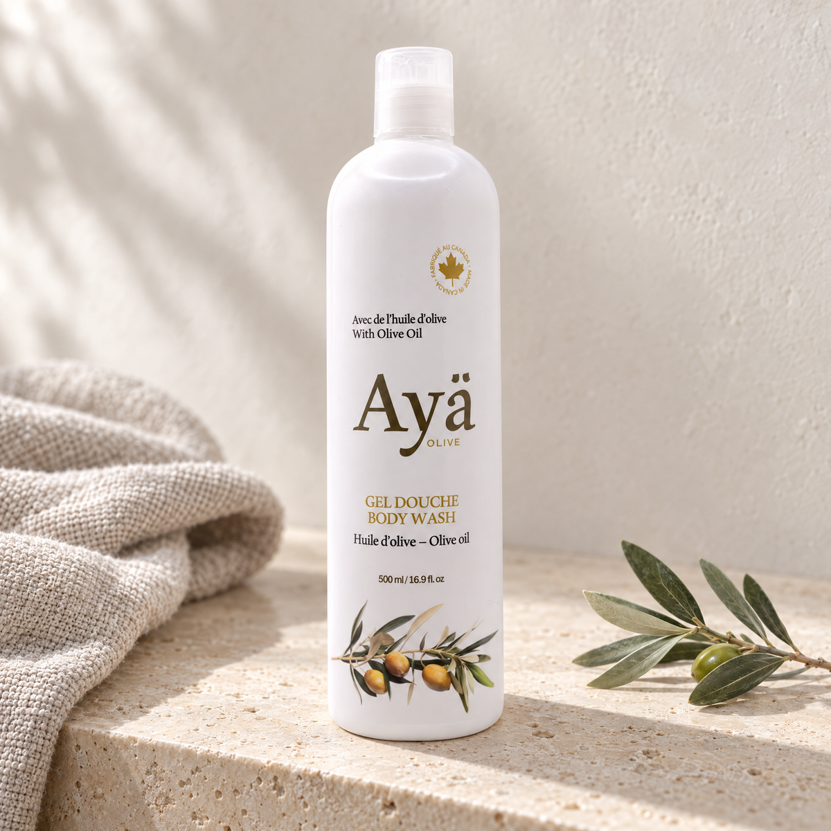 Ayä Olive body wash 500 ml bottle on a travertine bathroom ledge with linen towel and olive sprig