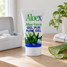 Aloex Aloe Vera pure topical gel 125g on a light oak table beside an open first-aid tin and a cut aloe vera leaf