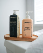 Caprina white tea & sage body lotion 500 ml with matching body wash on a wooden tray in a bright bathroom